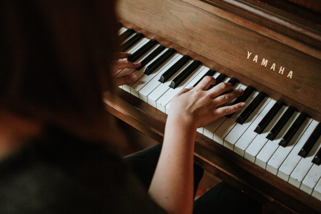 An above view of a woman's hands playing a brown Yamaha piano.