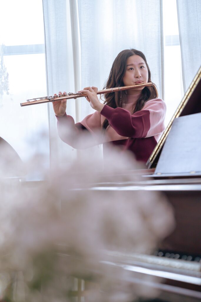 A woman playing the flute behind a grand piano.